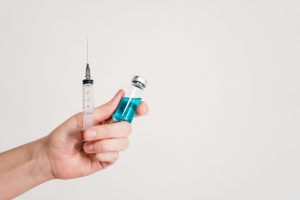 Hand holding a syringe and vaccine vial on a white background, symbolizing healthcare and immunization.
