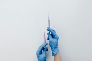 Close-up of blue gloved hands holding two medical syringes against a light background.